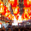 a little girl sitting on her father's shoulders with a tanghulu in right hand